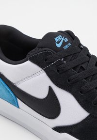 Tenisky Nike SB mají černý svršek z kůže a semiše s bílým plátnem a modrými akcenty, texturované tkaničky a gumovou podrážku.