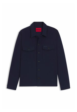 Camicia blu navy con bottoni realizzata in un tessuto liscio, dotata di due tasche sul petto e colletto. Logo mostrato sulla tasca sinistra superiore.