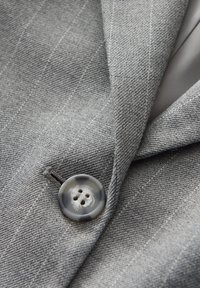 Gros plan sur le revers d'une veste de costume en tissu gris avec un grand bouton gris marbré cousu près de la boutonnière.