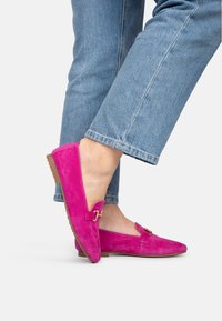 Fuchsia Wildleder Slipper mit niedrigem Profil, ausgestattet mit einer goldenen Schnallenakzent. Die Schuhe haben eine flache, beige Sohle und eine glatte, strukturierte Oberfläche.