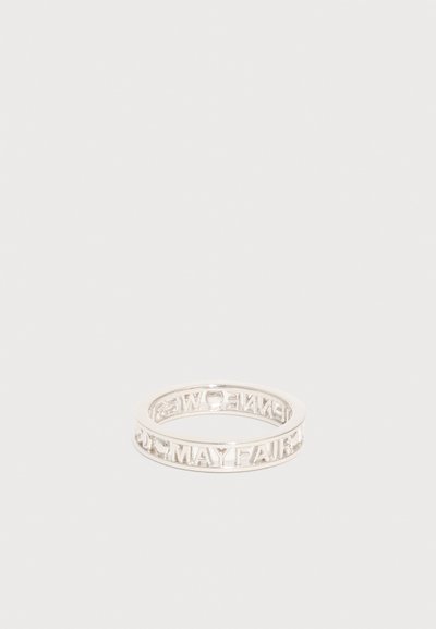 Ασημένιο δαχτυλίδι με ανοιχτό σκαλίζωμα που σχηματίζει τα γράμματα "MAY FAIR" και "KENNEDY" γύρω από τη στεφάνη σε λευκό φόντο.