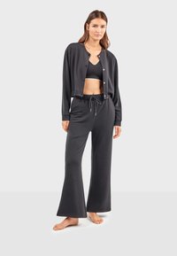 Schwarz aussehendes Loungewear-Set mit einer verkürzten Strickjacke mit Knöpfen und weiten Hosen mit verstellbarem Kordelzugbund. Glatte Stofftextur.