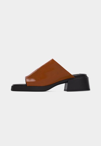 Mule marron à bout ouvert avec une large bride en cuir et un talon bas noir épais sur fond blanc.