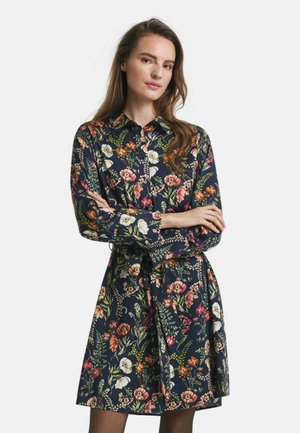 Abito camicia floreale con sfondo blu scuro, maniche lunghe, chiusura a bottoni sul davanti e vita legata, caratterizzato da un mix di motivi floreali colorati.