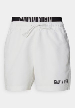 Hvite svømmeshorts med svart elastisk midjebånd med "CALVIN KLEIN"-logo. Materialet er lett og har en glatt tekstur.