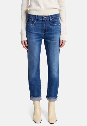 Jeans in denim blu con taglio dritto, leggera sfumatura, risvolti, e design a cinque tasche, abbinati a stivali alla caviglia color crema.