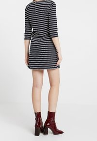 Randig klänning med trekvartsärmar i marinblått och vitt. Har en figursydd midja och bakdragkedja. Bärs med glänsande burgundy ankelstövlar.