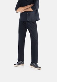 Chemise noire, légère, à manches courtes, avec un bouton, associée à un pantalon noir ajusté et des chaussures en cuir noires avec des semelles blanches.