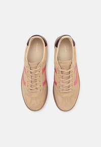 Sneakers in suede beige con strisce rosa, punta rotonda e lacci beige. L'interno presenta un rivestimento color crema e un dettaglio del logo dorato.