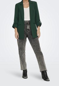 Mörkgrön blazer med uppvikta ärmar, kombinerad med högmidjade svart-och-vita jeans i denim. Svarta ankelskor med silveraccenter.