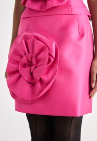 Klar rosa satendress med en stor blomst laget av stoff på siden, med en jevn tekstur og en tettsittende silhuett.