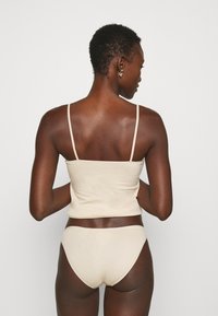 Beige Baumwoll-Cami mit dünnen Trägern und passenden Bikini-Briefen, die eine glatte Textur und ein einfaches, minimalistisches Design zeigen.
