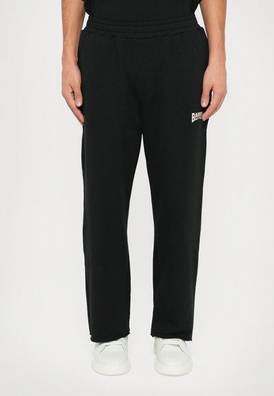 Un pantalon de survêtement noir avec une taille élastique, des poches latérales et un petit logo blanc de la marque sur la cuisse gauche. Fabriqué à partir d'un tissu doux et lisse.