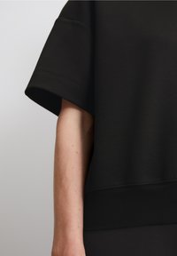 Černá krátká mikina z měkké látky s širokými krátkými rukávy a žebrovaným lemem. Hladká textura a minimalistický design.