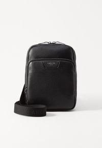 Sac en cuir noir à bandoulière avec une surface texturée, ferrures en argent, poche zippée à l'avant et sangle en tissu ajustable avec le logo "LANCEL".