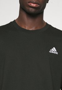 Svart bomulls-t-shirt med rund halsringning, korta ärmar och en vit Adidas-logotyp broderad på vänstra bröstet.