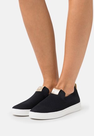 Scarpe slip-on in maglia nera con suole bianche, dotate di un accento dorato sul tallone e una superficie testurizzata. Progettate senza lacci.