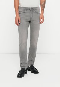 Jeans in denim grigio con vestibilità slim, design a cinque tasche e dettagli di cucitura sottili, abbinati a mocassini neri.