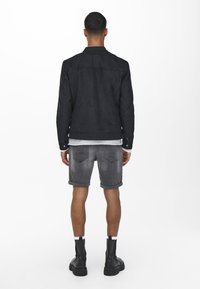Svart semsket skinnjakke med rett snitt og lett design. Kombinert med grå denimshorts med oppbrettede ermer og teksturert overflate. Sorte støvler fullfører looken.
