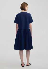 Marineblauwe jurk met korte mouwen, aansluitend lijfje en een uitlopende, geplooide rok. Gemaakt van zachte stof met een gladde textuur.