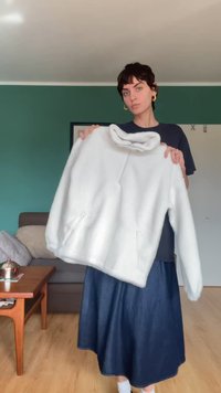 Sudadera de forro polar blanca y esponjosa con un cuello alto, bolsillos laterales con cremallera y una silueta amplia. Situada sobre un fondo verde.