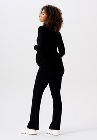 Haut noir à manches longues et pantalon ajusté assorti, avec un design décontracté. Tissu lisse, présentant des détails froncés sur les côtés, associé à des baskets blanches.