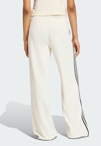 Bijele široke hlače izrađene od teksturiranog materijala, s crnim bočnim trakama i stražnjim džepom. Dizajn je prilagođen udobnosti i stilu.