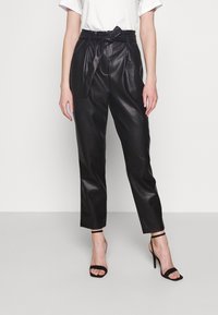 Pantalones de piel sintética negros con pliegues, cintura con cinturón y pierna ajustada. Combinados con tacones negros con tiras. Top blanco sencillo.
