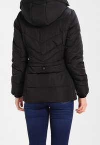 Giacca a piumino nera con cappuccio, caratterizzata da un quilting a chevron, una vita stirata e un dettaglio con bottone sul retro. Materiale liscio e resistente all'acqua.