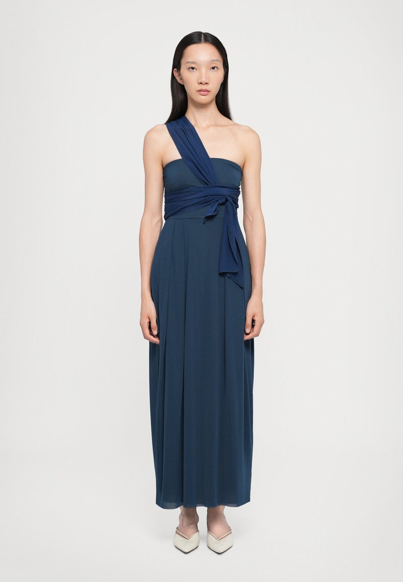 Navy blue, yhdestä olasta avonaista maxi-mekkoa, jossa on kiertynyt etuosa ja sidottu yksityiskohta. Sujuva, valunut kangas ulottuu nilkkoihin. Jalkineet ovat vaaleita.