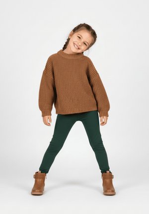 Brązowy dziergany sweter, zielone legginsy i brązowe botki za kostkę. Sweter ma luźny fason i szerokie rękawy. Miękki, teksturowany materiał.