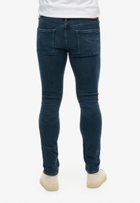 Jeans slim fit de color azul oscuro, fabricados en denim, con una cintura de altura media, bolsillos traseros y un acabado suave y ligeramente texturizado.