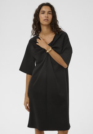Crna oversized haljina s kratkim rukavima, s dubokim V-izrezom i naborima sprijeda. Glatka tekstura tkanine, do koljena.