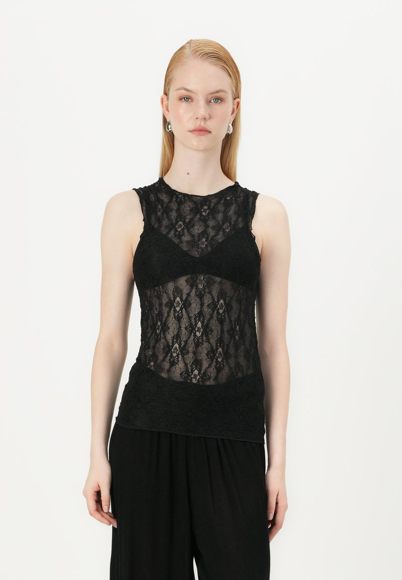 Svart blonde tanktop med en gjennomsiktig bodice, med intrikate diamantmønstre og solid svart kant. Modellen bruker den med løse svarte bukser.