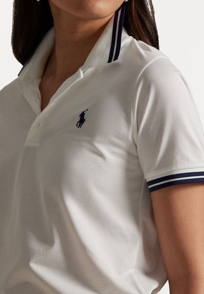 Biele polo tričko s krátkymi rukávmi, s tmavomodrým pruhovaným golierom a malým tmavomodrým logom na hrudi. Texturovaná tkanina.