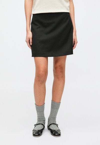 Minigonna nera con una texture liscia, abbinata a calzini grigi a coste e scarpe nere con dettagli decorativi in metallo.