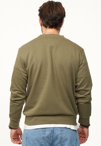 Olive green sweatshirt with a textured, ribbed fabric. Features long sleeves, round neckline, and a fitted waistband. Back view displayed.
