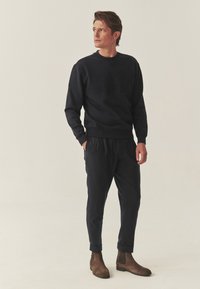 Granatowa bluza z dzianiny z wytłoczonym logo, zestawiona z granatowymi, zwężanymi spodniami i brązowymi zamszowymi botkami za kostkę. Prosty fason o luźnym kroju.