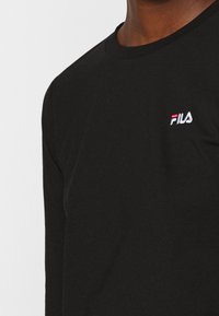 Svart långärmad t-shirt i bomull. Har en liten broderad FILA-logotyp i vitt och rött på vänster bröst. Mjuk textur.