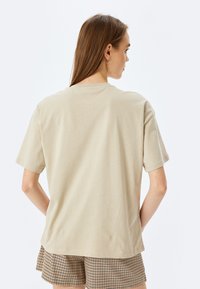 Beige kortærmet t-shirt med rund halsudskæring. Glat bomuldsstof, afslappet pasform, ingen synlige mønstre eller bemærkelsesværdige accenter.