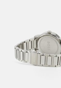 Reloj de acero inoxidable plateado con un acabado cepillado, que presenta un diseño de pulsera de eslabones y una caja redonda con una corona pulida.