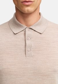 Beige gestricktes Polohemd mit klassischem Kragen und drei hellrosa Knöpfen an der Knopfleiste. Weicher Stoff und taillierte Passform.