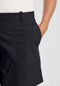 Zwarte shorts met een gladde textuur, voorzien van een zijzak en een tailleband. De stof is lichtgewicht en iets geraffineerd aan de zijkanten.