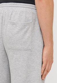 Hellgraue Sweatpants aus strukturiertem Stoff, mit elastischem Bund und einer Gesäßtasche. Das Design ist locker geschnitten und hat ein gerades Bein.