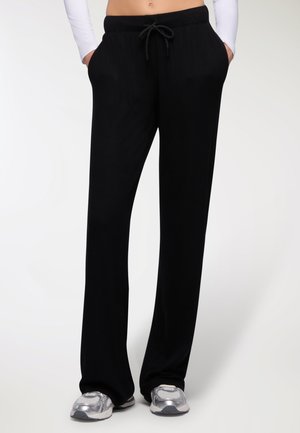 Pantaloni lounge neri a costine con vestibilità rilassata, vita con cordino, tasche laterali e texture morbida. Abbinati a scarpe da ginnastica argentate.