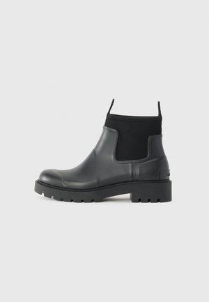 Bottine en cuir noir avec panneaux latéraux élastiques, languettes, semelle crantée épaisse et talon bloc bas, vue de profil.