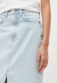 Lyseblå denimskjørt med frontspalte, sidelommer og fremtredende sømmer, i en høy påsydd design.