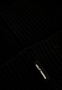 Czarna prążkowana tkanina o miękkiej fakturze. Posiada białą metkę "Helly Hansen" na czarnym tle.