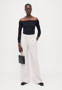 Svart off-the-shoulder långärmad topp kombinerad med högmidjade, vida ljusbeiga byxor. Tillbehör inkluderar en liten svart handväska.