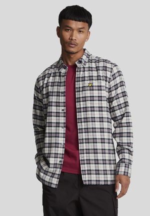 Camisa de cuadros en blanco, azul marino y burdeos, superpuesta sobre una camiseta burdeos. Presenta un pequeño logo bordado en amarillo en la camiseta.